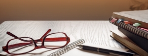 Study Hall glasses folded on an open notebook with a pen and stack of books to the right